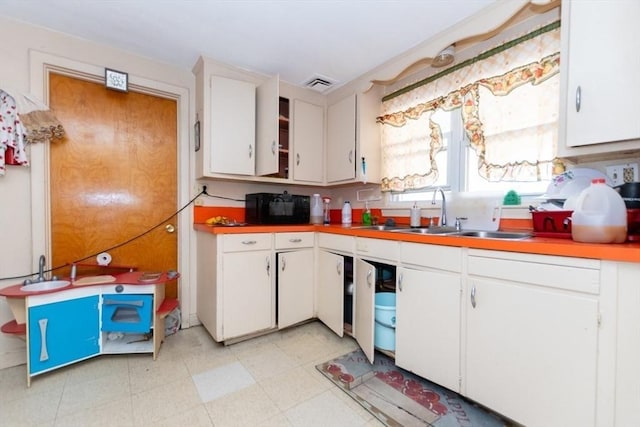 kitchen featuring light floors, light countertops, visible vents, white cabinets, and a sink