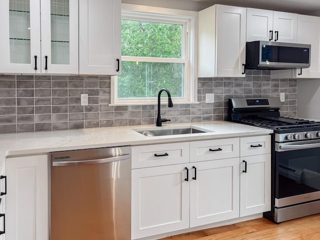 624 Western Ave, Gloucester, MA 01930 - kitchen with stainless steel appliances, white cabinetry, light stone countertops, glass insert cabinets, and decorative backsplash