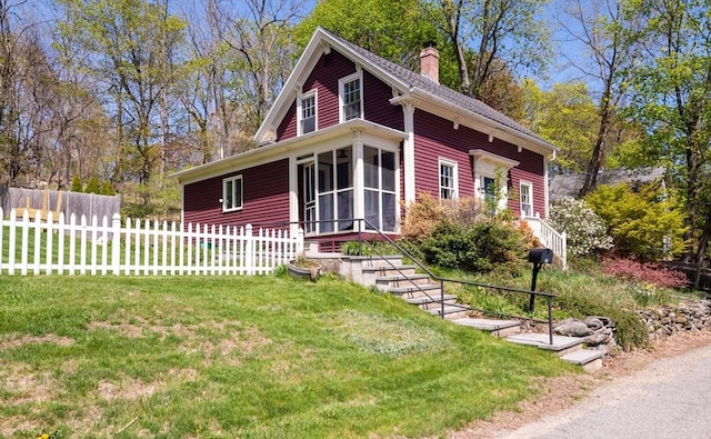 view of front facade featuring fence, a sunroom, a chimney, and a front yard