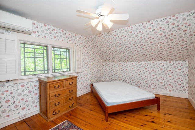 bedroom featuring a wall mounted air conditioner, ceiling fan, baseboards, wallpapered walls, and light wood-style floors