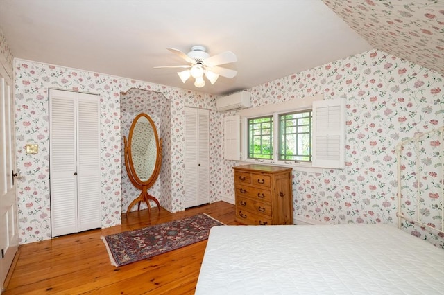 bedroom featuring wallpapered walls, wood finished floors, multiple closets, and a wall mounted air conditioner