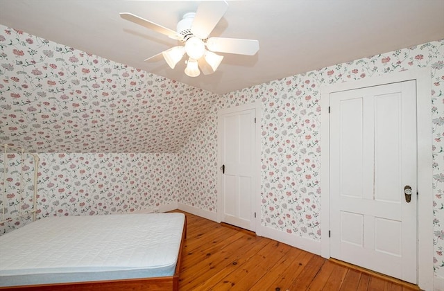 unfurnished bedroom featuring baseboards, wood-type flooring, and wallpapered walls
