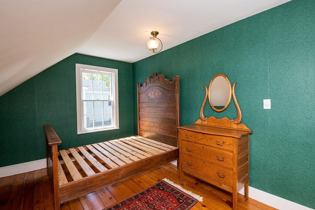 bedroom with baseboards, lofted ceiling, and hardwood / wood-style floors