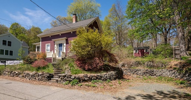 view of front facade featuring a storage shed, a chimney, and an outbuilding