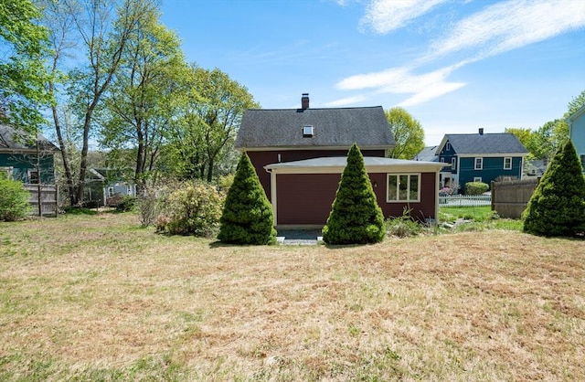 rear view of house with a lawn, a chimney, and fence