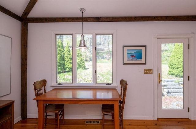 dining room with baseboards, a healthy amount of sunlight, beam ceiling, and wood finished floors