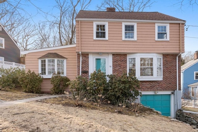 colonial inspired home featuring brick siding, an attached garage, a chimney, and fence