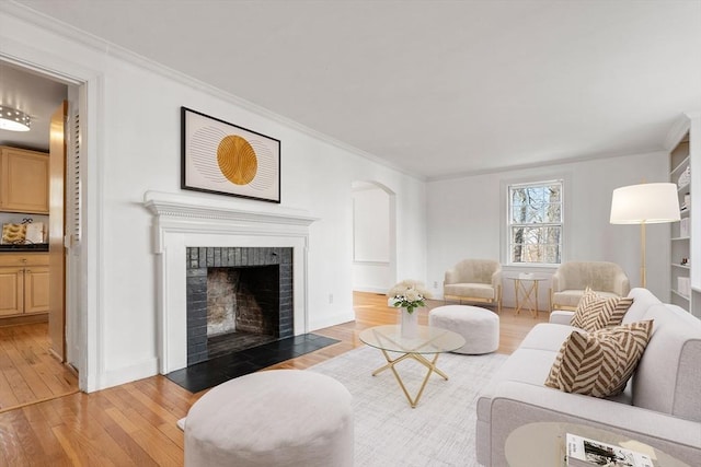 living room with arched walkways, light wood-style floors, ornamental molding, and a fireplace