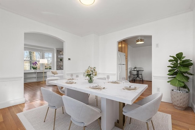 dining area featuring light wood-type flooring, arched walkways, and crown molding