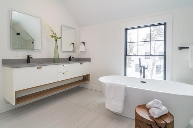 bathroom featuring double vanity, lofted ceiling, a soaking tub, a sink, and tile patterned flooring