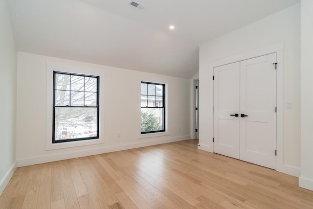 unfurnished bedroom with light wood-style floors, baseboards, visible vents, and vaulted ceiling