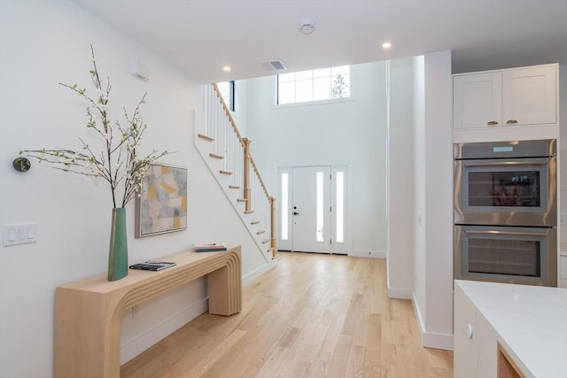 foyer with recessed lighting, a towering ceiling, visible vents, light wood-style floors, and stairway