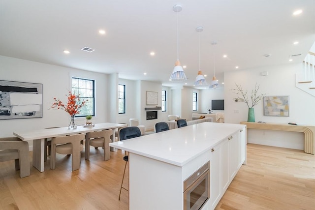 kitchen with white cabinets, stainless steel microwave, open floor plan, hanging light fixtures, and light countertops