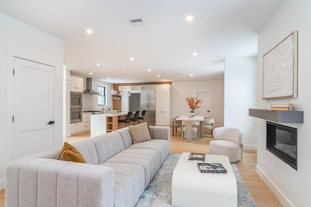 living room with light wood-type flooring, a glass covered fireplace, and recessed lighting