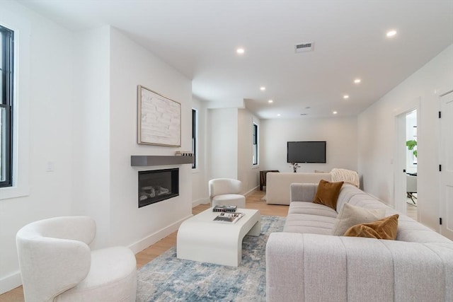 living room with light wood-type flooring, a glass covered fireplace, visible vents, and recessed lighting