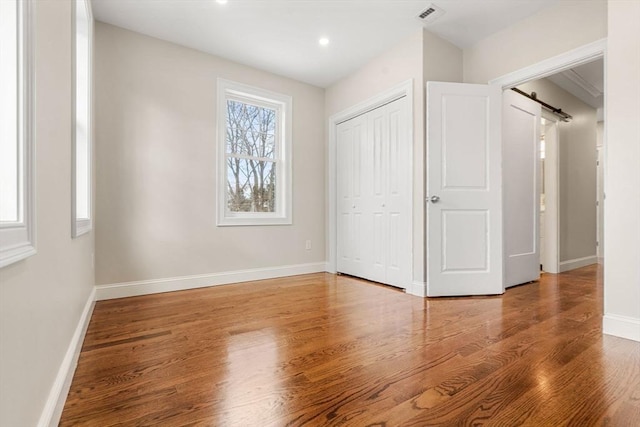 unfurnished bedroom with a closet, hardwood / wood-style flooring, and a barn door