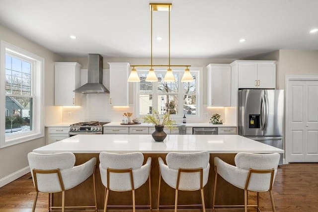 kitchen featuring wall chimney exhaust hood, stainless steel appliances, white cabinetry, a center island, and a healthy amount of sunlight