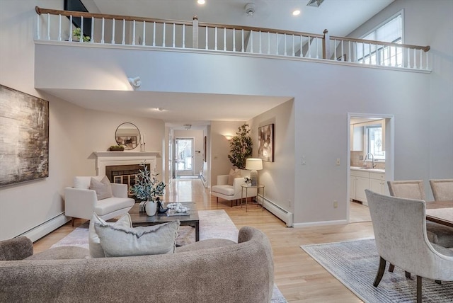 living room with baseboard heating, a glass covered fireplace, light wood-style flooring, and baseboards