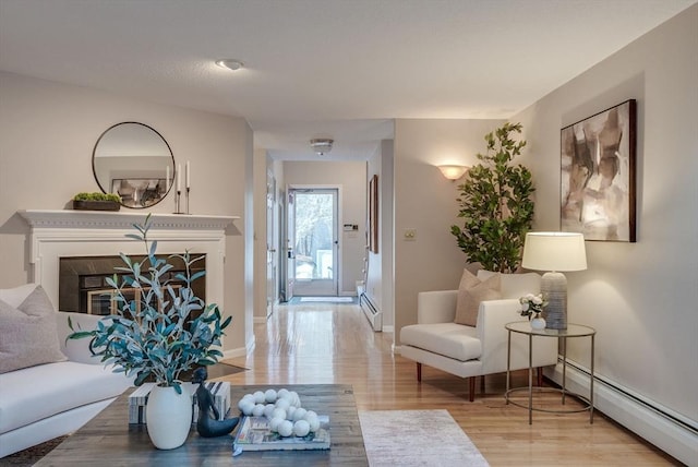 living area featuring a baseboard heating unit, a glass covered fireplace, light wood-style flooring, and baseboards