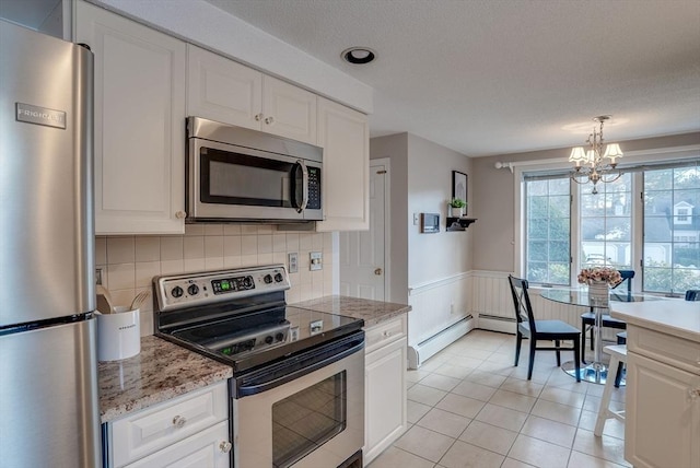 kitchen with light tile patterned floors, white cabinets, wainscoting, a baseboard radiator, and appliances with stainless steel finishes