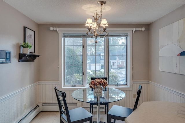 dining area featuring a textured ceiling, baseboard heating, wainscoting, and a notable chandelier