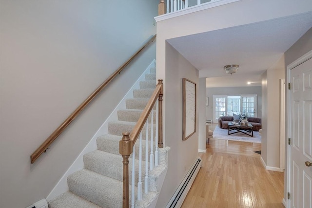 stairs with baseboard heating, wood finished floors, and baseboards