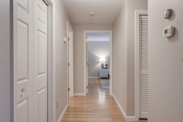 hall featuring a textured ceiling, light wood-type flooring, and baseboards