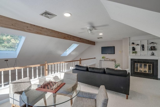 carpeted living room featuring vaulted ceiling with skylight, visible vents, ceiling fan, and a fireplace with flush hearth