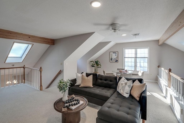 carpeted living area with a textured ceiling, lofted ceiling with skylight, visible vents, and a ceiling fan