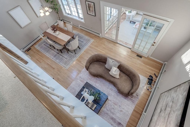 living area with a chandelier, visible vents, baseboard heating, and wood finished floors