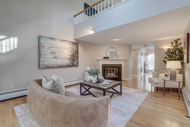 living room with light wood finished floors, baseboard heating, and a fireplace with flush hearth