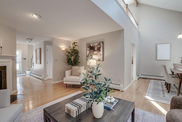 living area featuring a baseboard heating unit, light wood-type flooring, a fireplace, and baseboards