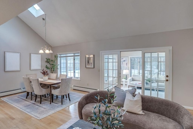 dining area with a baseboard heating unit, vaulted ceiling with skylight, light wood-type flooring, and a notable chandelier