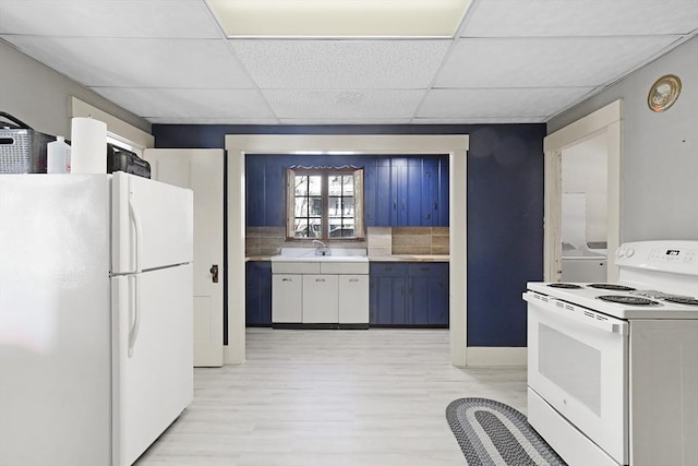 kitchen featuring a paneled ceiling, white appliances, a sink, light countertops, and light wood-type flooring