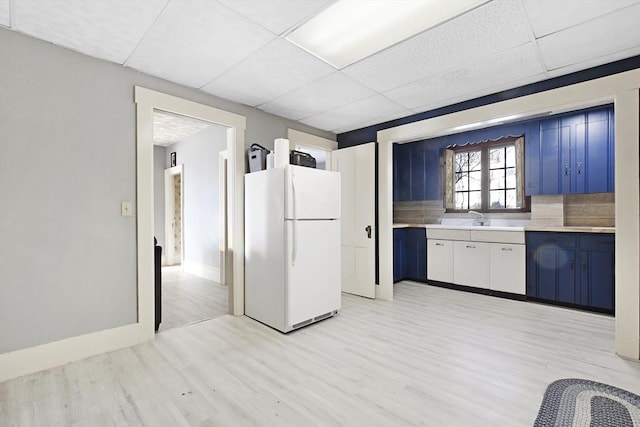 kitchen with light countertops, freestanding refrigerator, blue cabinets, light wood-type flooring, and a drop ceiling