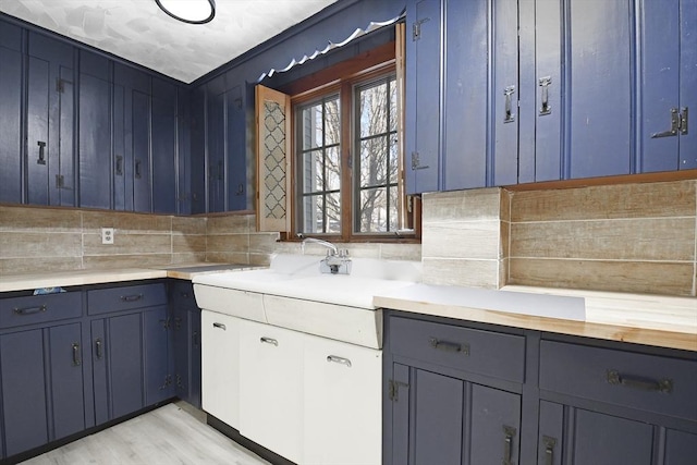 kitchen with light countertops, blue cabinetry, light wood-type flooring, and decorative backsplash