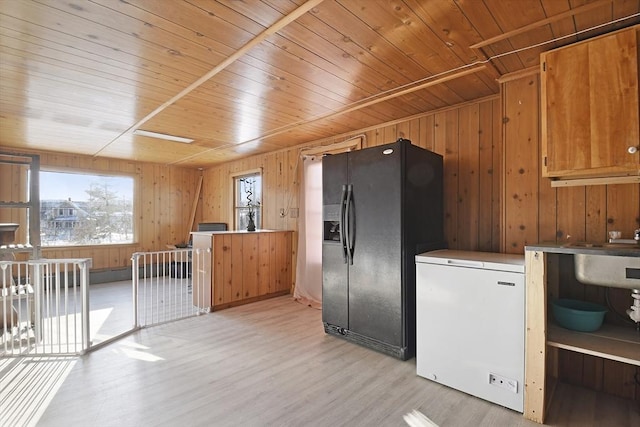 kitchen with wood walls, black fridge, fridge, and light wood-style flooring