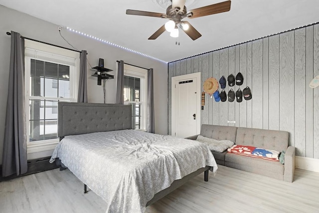 bedroom featuring multiple windows, wood finished floors, a ceiling fan, and wooden walls