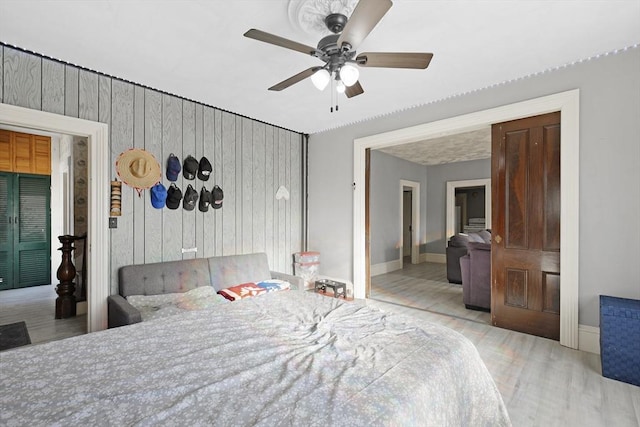 bedroom featuring ceiling fan, wood walls, baseboards, and wood finished floors