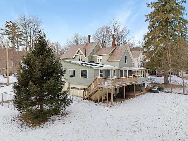 snow covered house featuring a garage, a sunroom, stairway, fence, and a wooden deck