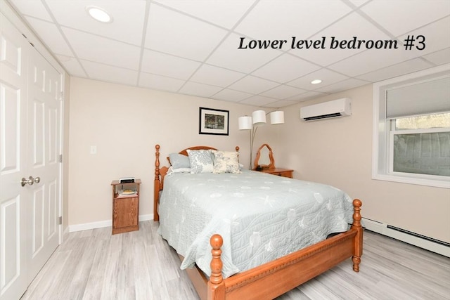 173 Standish Rd, Bourne, MA 02562 - bedroom with an AC wall unit, a paneled ceiling, light wood finished floors, baseboards, and baseboard heating