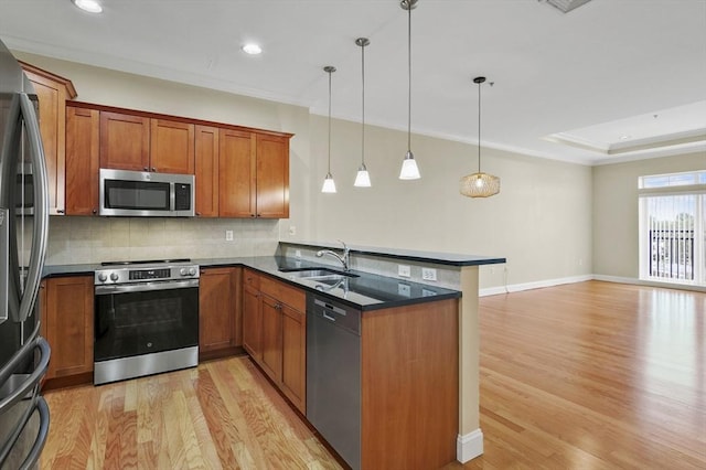 kitchen with stainless steel appliances, a sink, a peninsula, light wood finished floors, and brown cabinetry