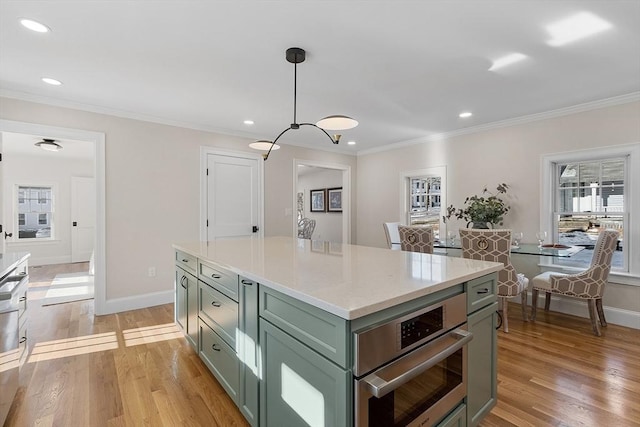 kitchen with light hardwood / wood-style flooring, a center island, hanging light fixtures, green cabinetry, and crown molding