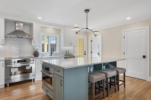 kitchen with appliances with stainless steel finishes, hanging light fixtures, a kitchen island, wall chimney exhaust hood, and white cabinets