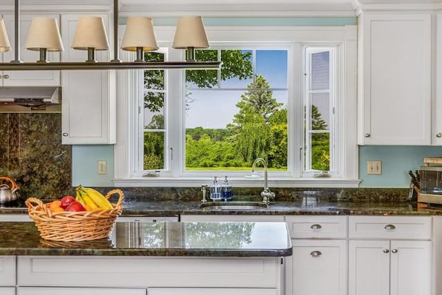 kitchen with white cabinets, dark stone countertops, a healthy amount of sunlight, and a sink