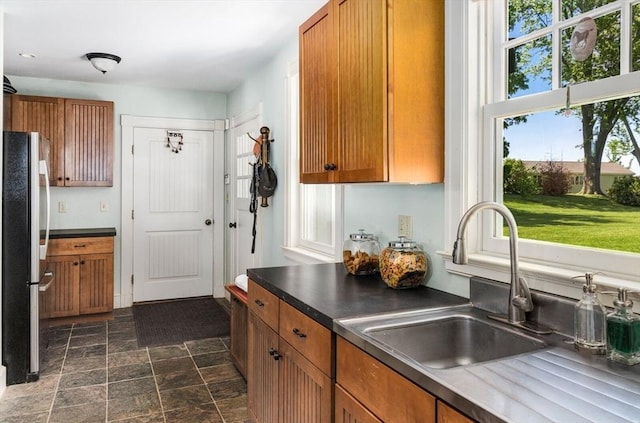 kitchen featuring freestanding refrigerator, brown cabinets, stone finish flooring, and a sink