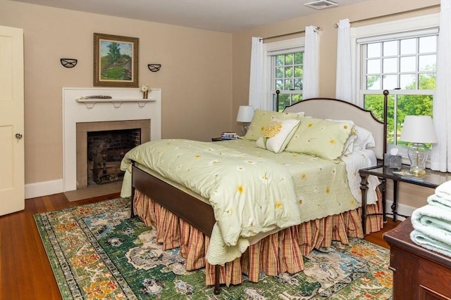 bedroom with baseboards, a fireplace with flush hearth, visible vents, and wood finished floors