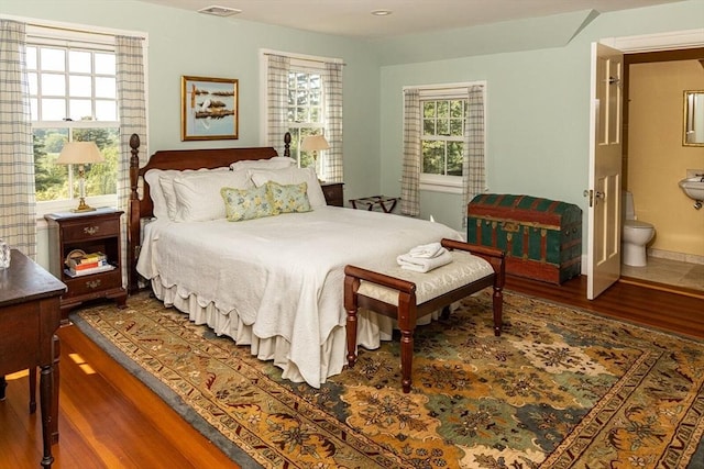 bedroom featuring ensuite bath, baseboards, visible vents, and wood finished floors