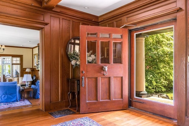 foyer entrance with crown molding, light wood-style flooring, and wooden walls