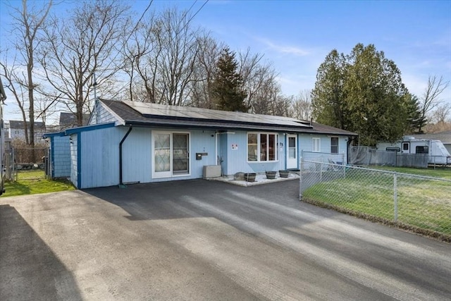 ranch-style home featuring a front lawn, fence, and roof mounted solar panels